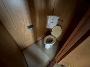 木目壁の狭いトイレと古い洋式便器